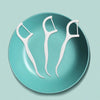 Three white reusable dental flossers resting on a teal ceramic plate.