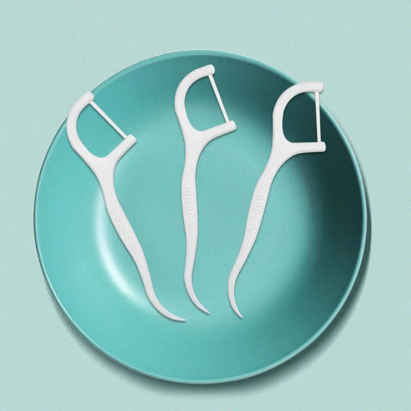 Three white reusable dental flossers resting on a teal ceramic plate.