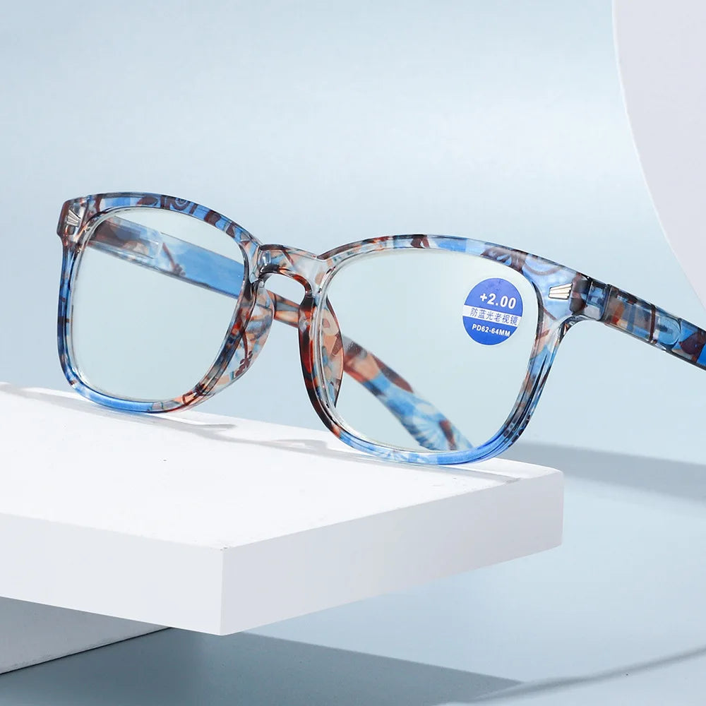 Pair of blue and brown patterned reading glasses resting on a white block.