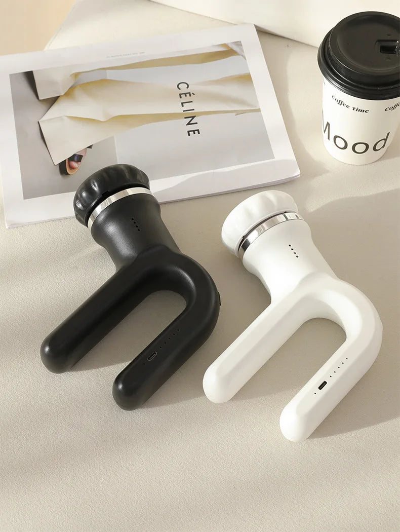 Eine schwarz-weiße 4-in-1 kabellose Massagepistole neben einer Kaffeetasse auf einer hellen Oberfläche.