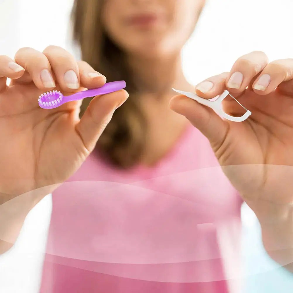 A person holds a purple toothbrush and a white dental flosser against a pink shirt.