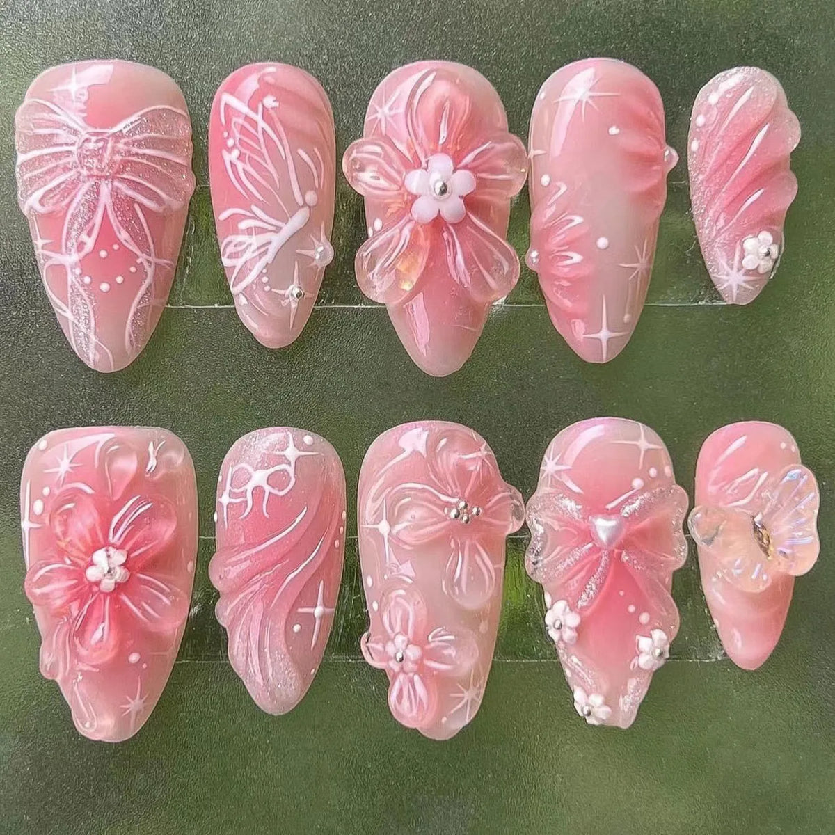 A set of 24 pink heart pearl press-on fake nails displayed on a green background.