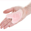 Una mano sostiene un trozo de cera rosa en forma de corazón para masaje facial.