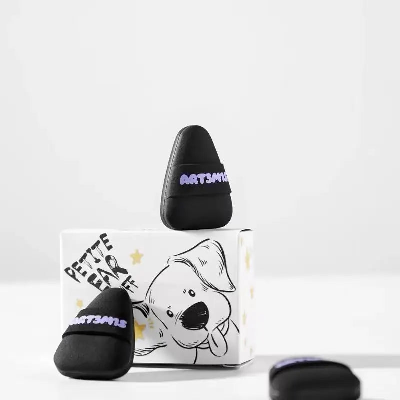Un tampon cosmétique noir à flockage avec un motif d'étoile jaune, à côté de son emballage.