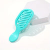 A light blue silicone mini travel hair brush with flexible bristles is shown next to its white packaging box.