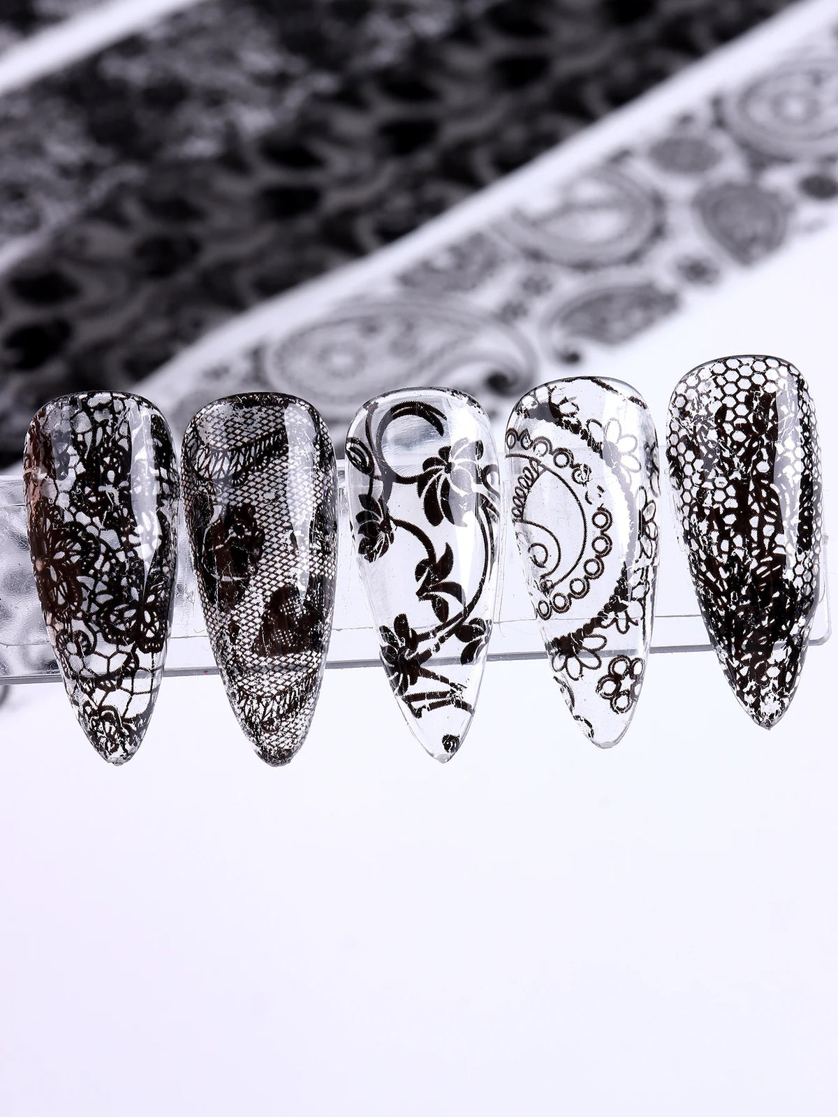 Un ensemble de autocollants pour ongles en foil de dentelle avec des motifs floraux blancs et noirs complexes sur des pointes