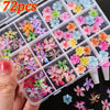 A hand holds an open clear plastic box filled with colorful floral resin nail charms featuring hibiscus flowers in various sh