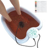 A person is using an ionic detox foot spa massager to soak their feet in reddish water.
