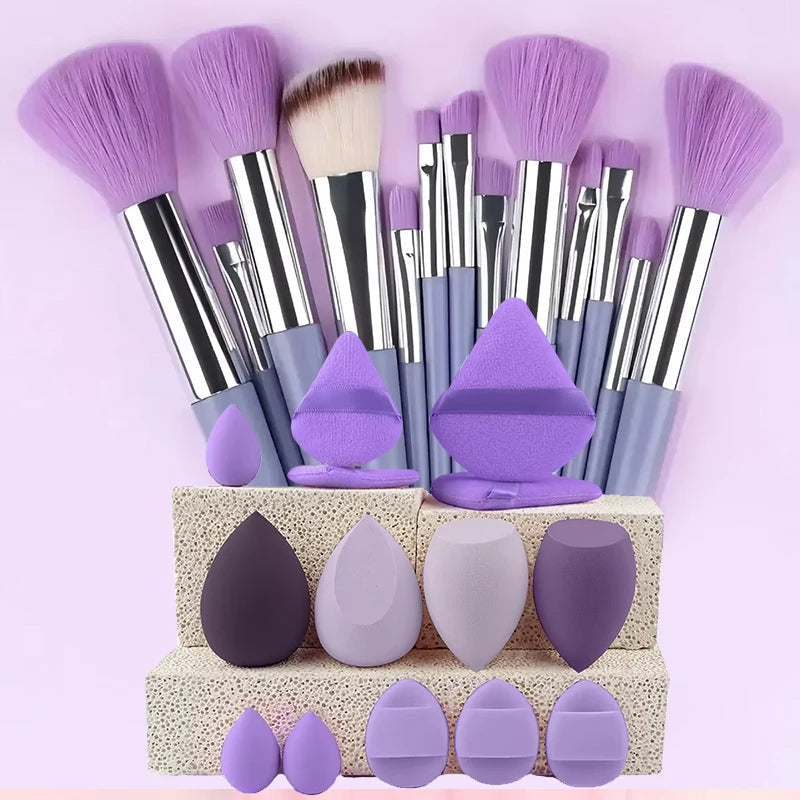 Una colección de doce brochas de maquillaje profesional en tonos morados y lila, exhibidas en una caja de color claro.