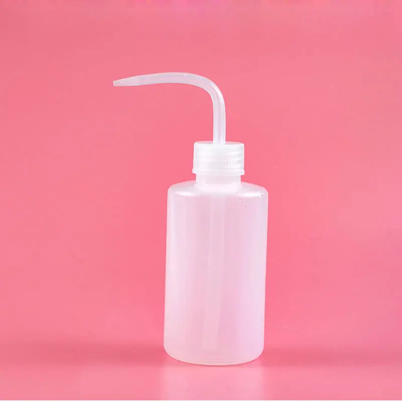 A clear plastic bottle for eyelash extension cleaning with a curved applicator brush against a pink background.