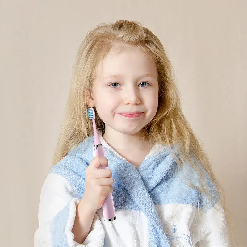 A young girl smiling while holding a pink ultrasonic electric toothbrush with replacement heads.