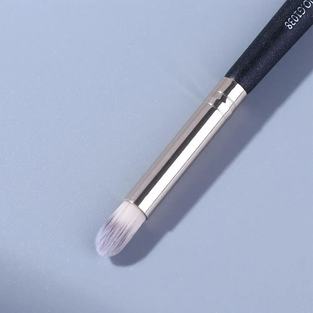 A close-up of a black and silver double-ended eye shadow brush with a smudge tip and blending shader on a light blue backgrou