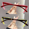A pair of pink cat eye reading glasses with thick frames and clear lenses being held by a hand.