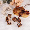 A collection of non-slip hat claw clips in a tortoiseshell pattern displayed on a wooden surface with soft white fur and rose