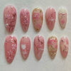 A collection of 24 pink heart pearl press-on fake nails featuring floral designs and glitter accents.