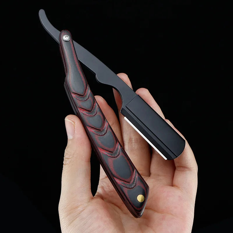 Una mano sostiene una maquinilla de afeitar manual negra y roja con mango texturizado contra un fondo oscuro.