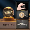A hand holds a glowing crystal ball night light displaying a galaxy pattern on a wooden base.