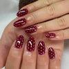 A hand displays a set of deep red pink striped press-on nails with an almond shape.