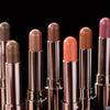A row of cosmetic eyeshadow sticks in various shades, including bronze, orange, and pink, displayed against a black backgroun