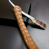 Afeitadora manual de madera con mango estampado y cuchilla plateada sobre una superficie oscura.