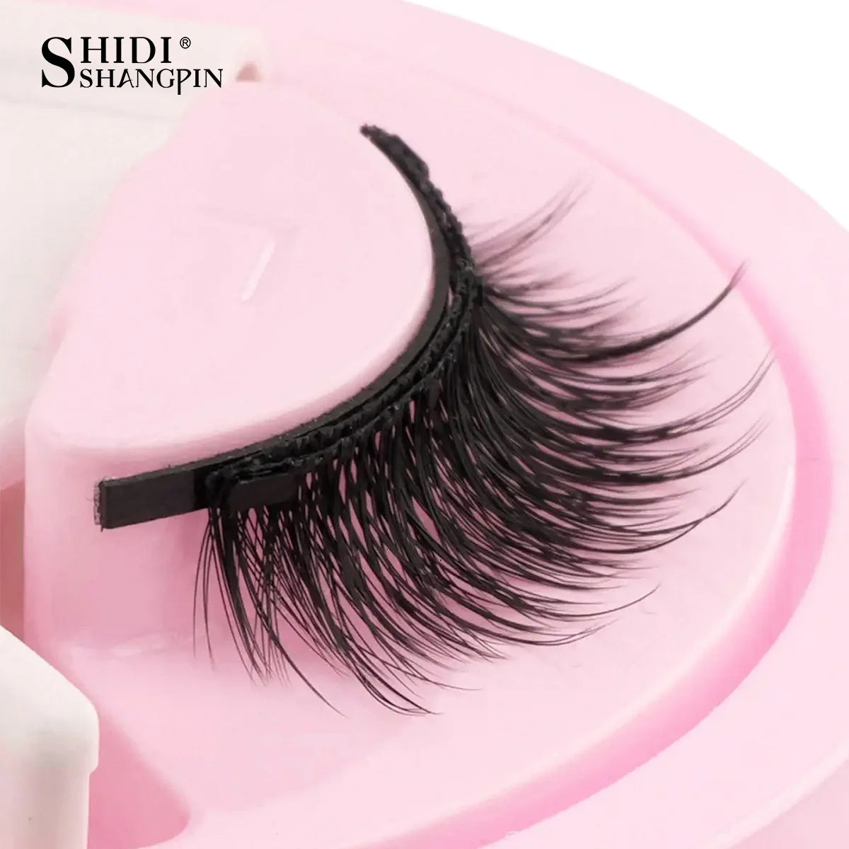 Gros plan d'une bande de faux cils magnétiques noirs sur un outil cosmétique rose.