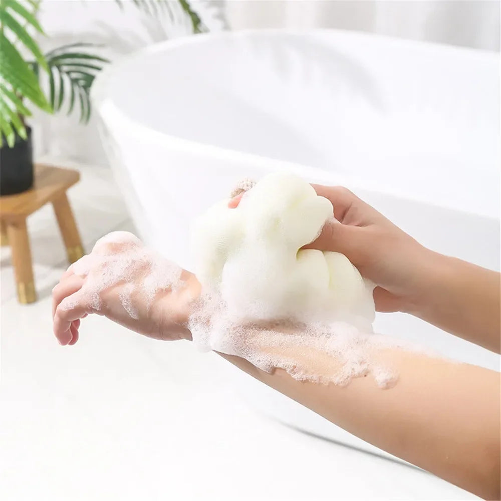 A hand is squeezing a white exfoliating bath bubble ball onto the palm of another hand.
