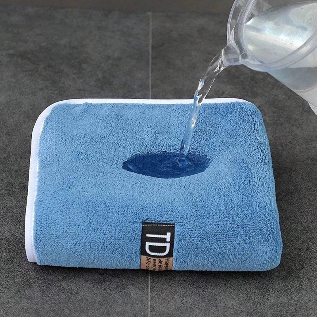 A blue microfiber cleaning towel is being wet by water from a glass.