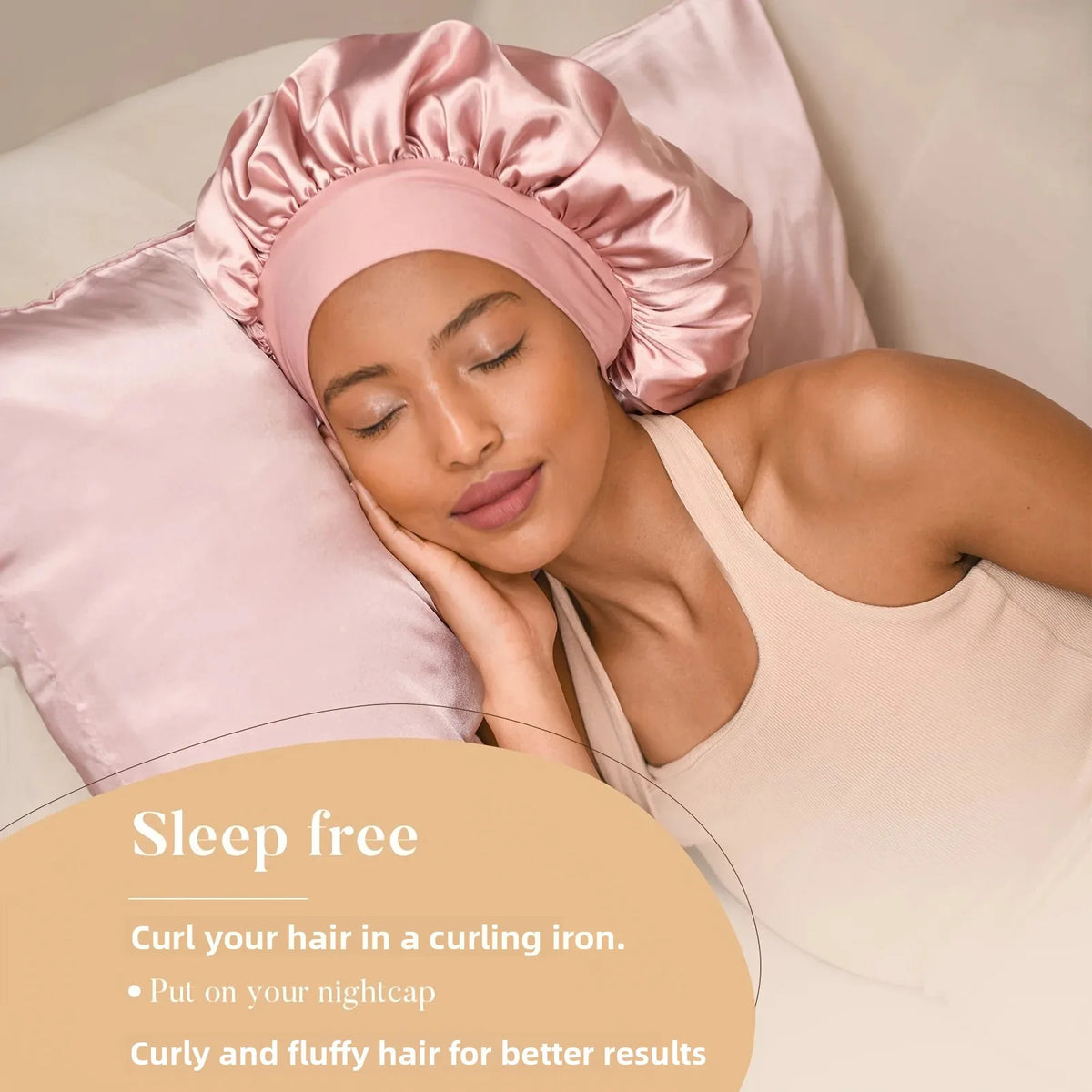 A woman is shown wearing a pink satin sleep cap and a beige tank top, with a pink satin hair cap resting on a pillow.