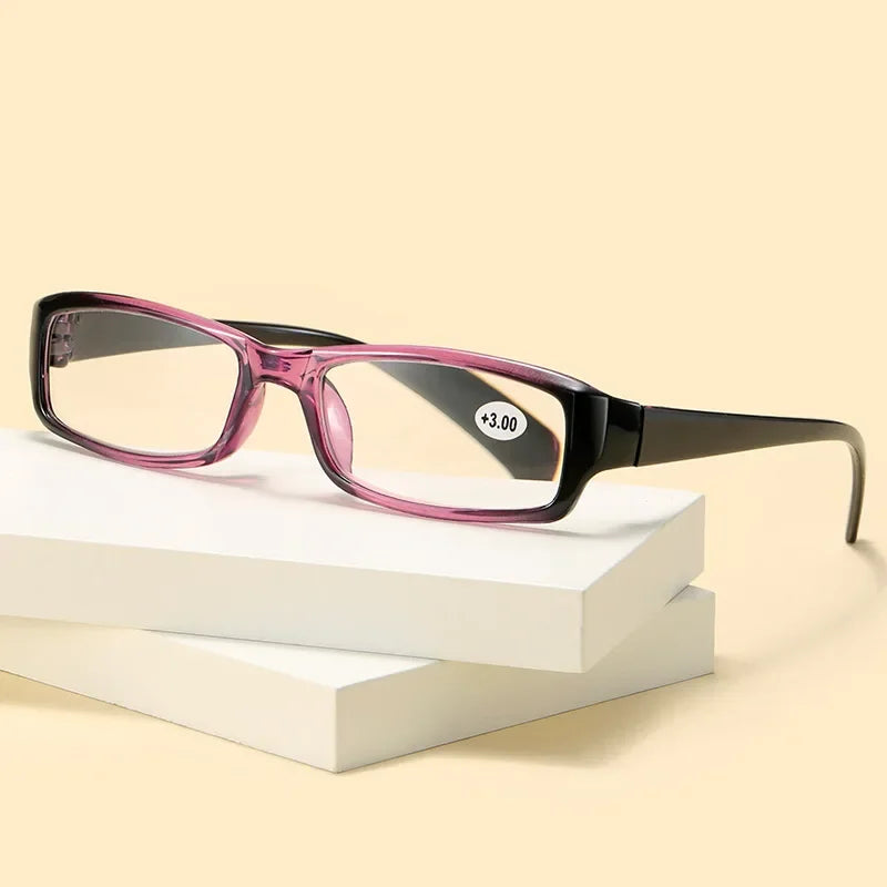 A pair of pink-framed reading glasses with clear lenses resting on a white block.
