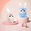 A light blue owl-shaped electric toothbrush for kids with a white brush head and a pink stand.