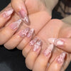 A close-up of hands displaying pink heart pearl press-on fake nails on fingers.