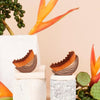 A set of wooden and natural fiber face brushes displayed on a white surface with orange floral elements.
