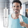 A man holds a portable USB rechargeable water flosser device with a clear water bottle and a detachable tip.