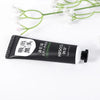 Un tubo de mascarilla exfoliante para puntos negros, con un tallo de planta verde de fondo.
