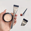 A hand holds an Ultra-Fine Oval Foundation Brush for Flawless Contouring, showing the brush and a compact foundation product.