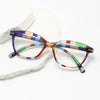 Pair of retro cat eye reading glasses with multicolored frames resting on a white stone.
