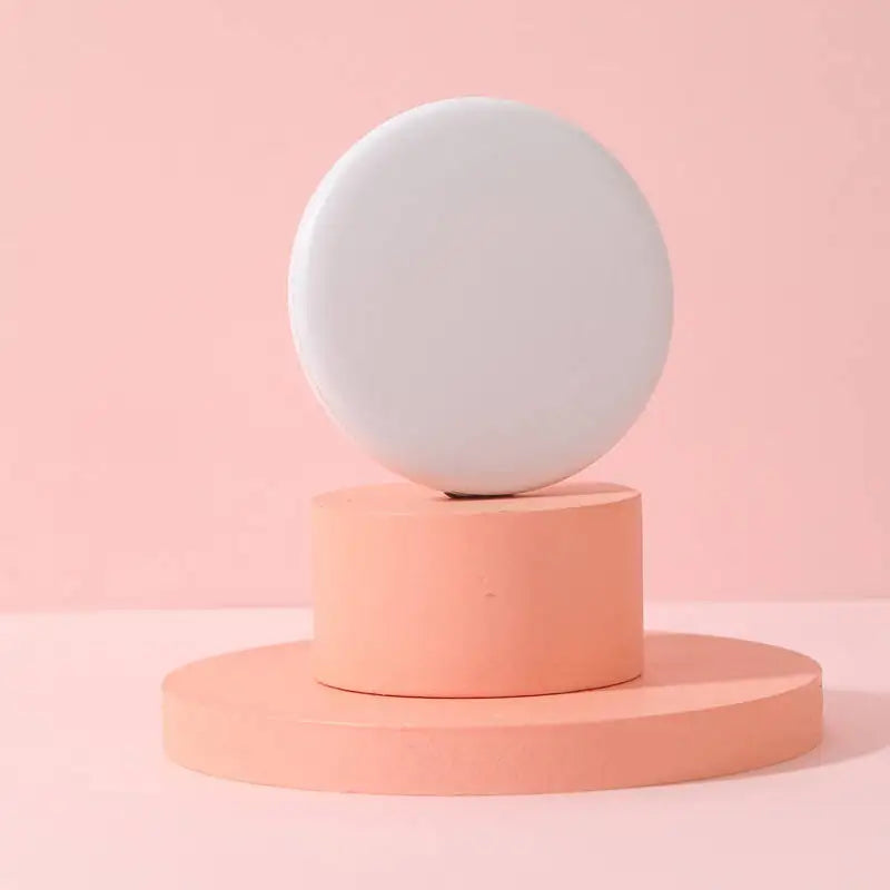 A round, white LED makeup mirror rests on a light coral pink stand against a pale pink background.