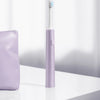 A purple sonic electric toothbrush with a white brush head stands on a white surface.
