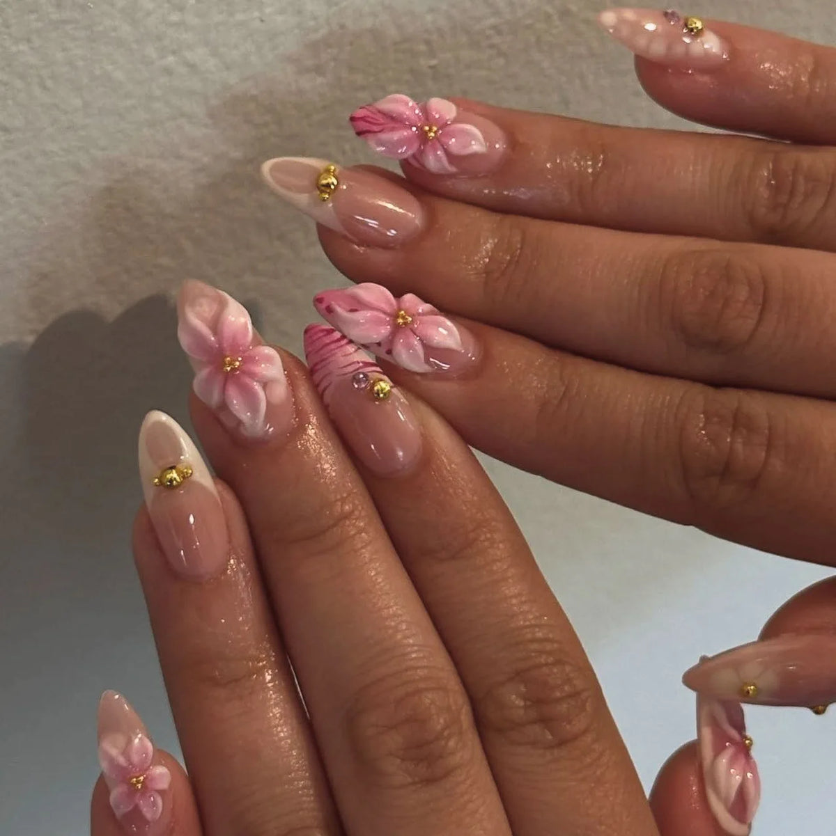 A close-up of hands displaying 24-piece almond press-on nails featuring pink floral and butterfly designs.