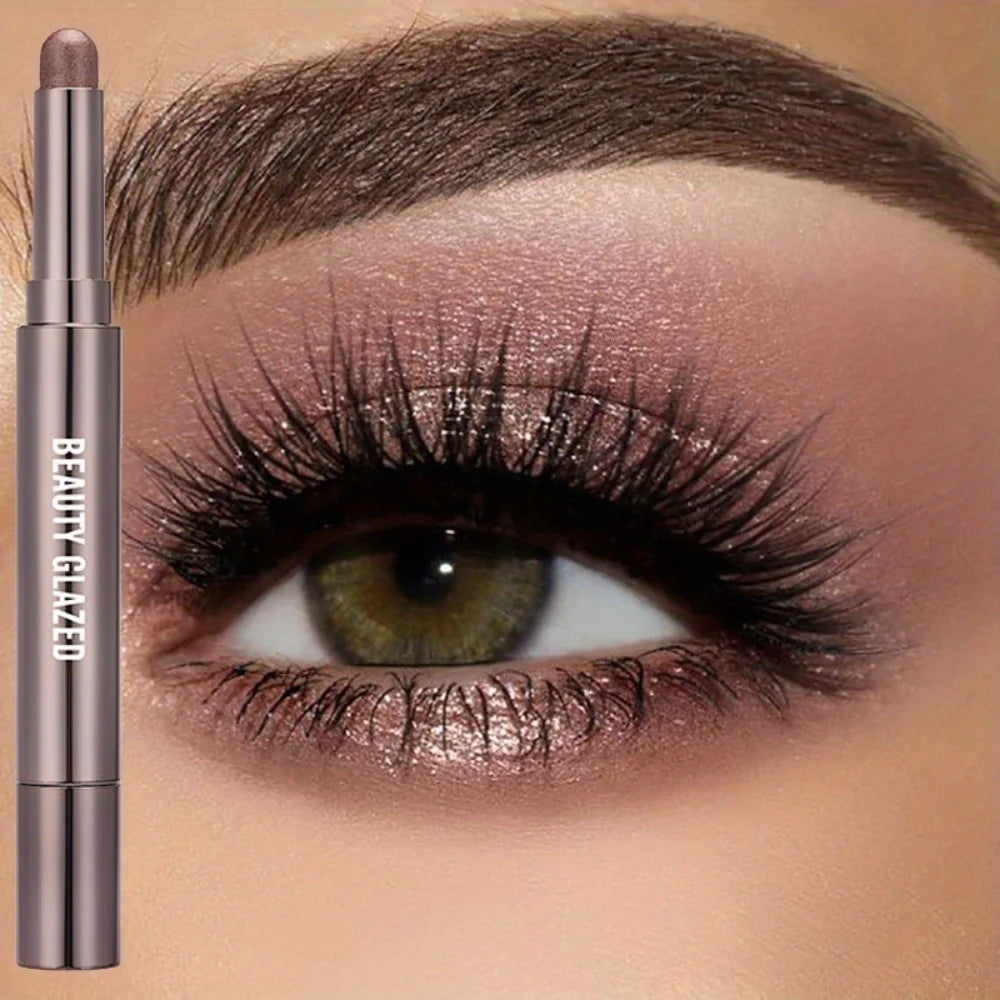 A cosmetic product featuring a long-lasting eyeshadow stick with a double brush shown next to an eye.