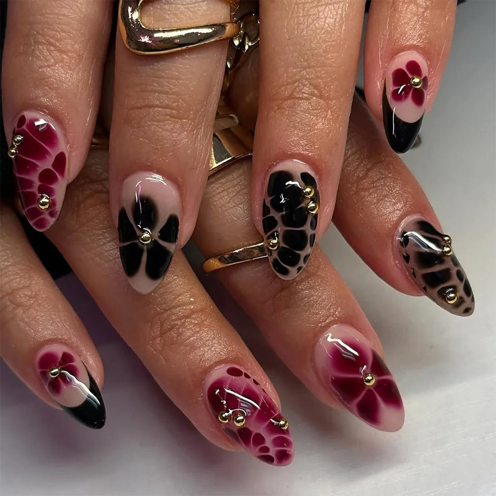 A close-up of a hand displaying various press-on nails featuring floral and butterfly designs in shades of pink, black, and w