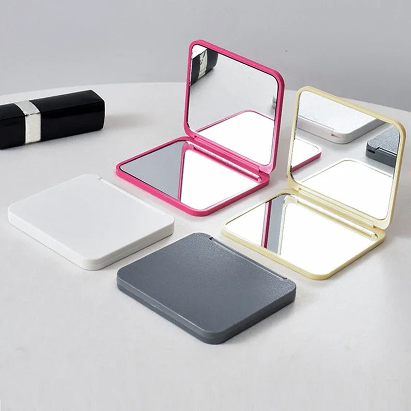 A set of double-sided portable makeup mirrors in pink, gold, and gray colors displayed on a white surface.