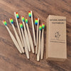 Une boîte contenant un pack de 10 brosses à dents en bambou naturelles à poils colorés, posées sur une surface en bois.