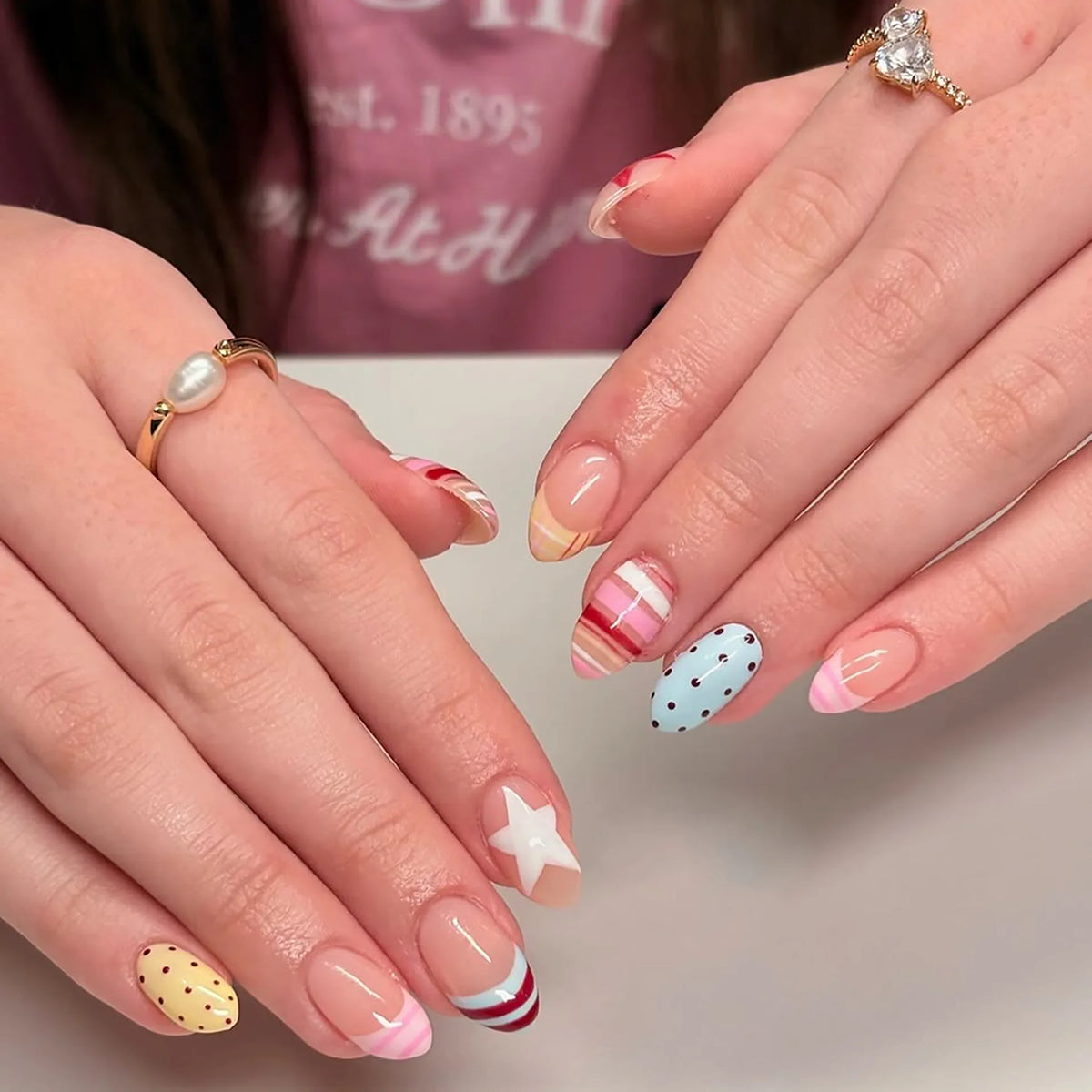 Close-up of hands displaying red pink striped press-on nails with almond shape and various designs