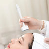 A hand is using an adjustable microneedle device on a person's skin or hair.