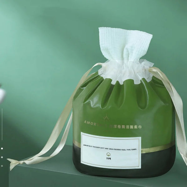 A green plastic bag filled with white soft cotton disposable face towels tied with a light beige ribbon.