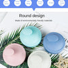 A set of round scalp massage brushes in various pastel colors, including blue, pink, and white, displayed on green palm leave