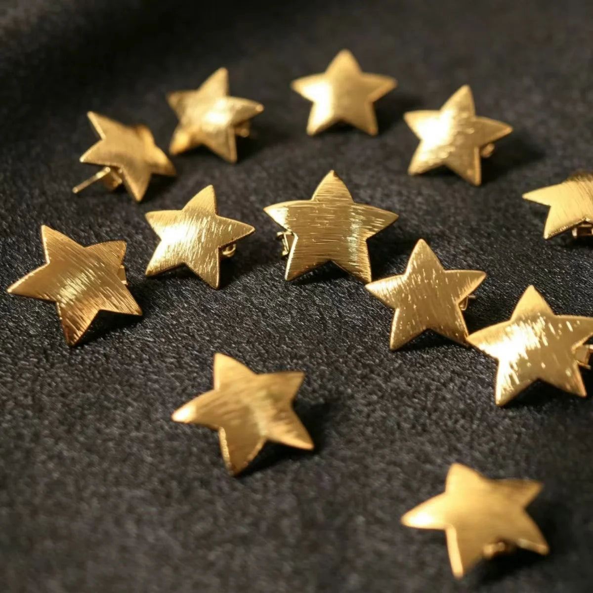 A collection of ten gold star-shaped hairpins scattered on a dark surface.