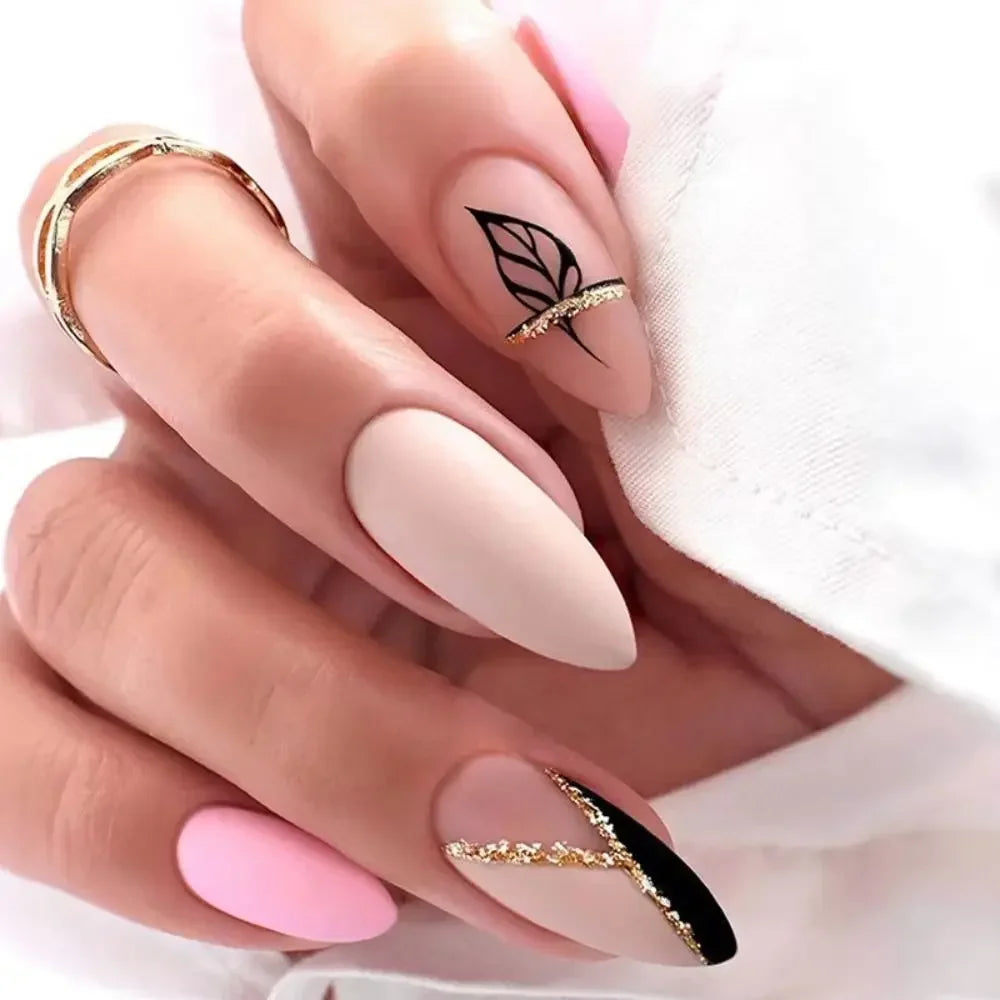A hand displaying press-on false nails with gold accents and a black leaf design on a light pink background.