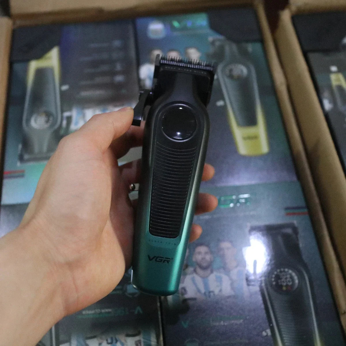 A hand holds a VGR professional cordless hair clipper with ceramic blades in a dark green casing.